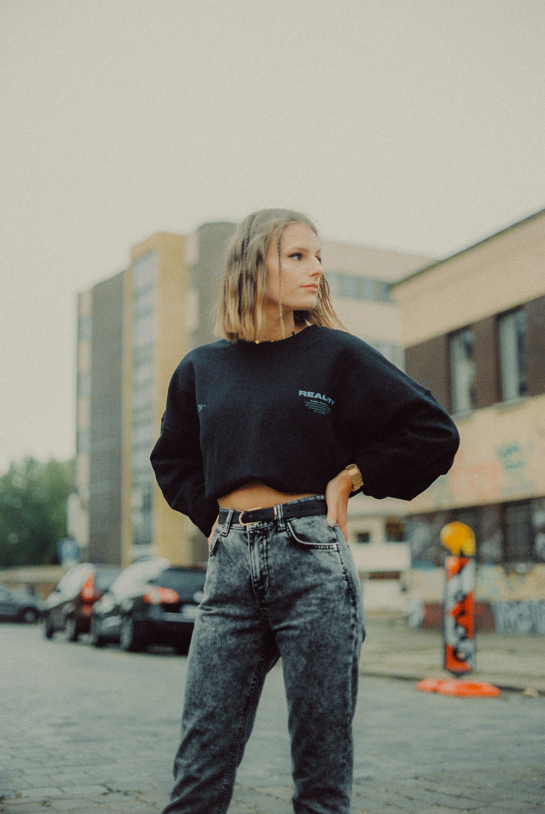 woman in black sweater and blue denim jeans standing on street during daytime